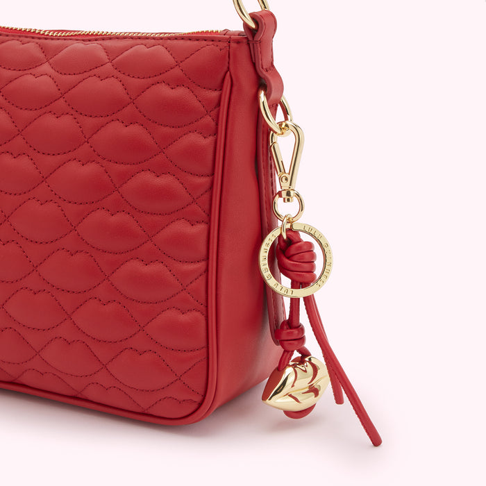 Close-up of a red quilted Lulu Guinness handbag with a gold lip-shaped charm attached.