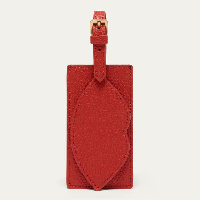 A red textured leather luggage tag with a matching strap and gold-tone buckle, displayed against a light off-white background.