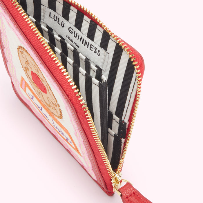 Red Lulu Guinness zip-around purse open to reveal its black and white striped interior and biscuit-themed design.