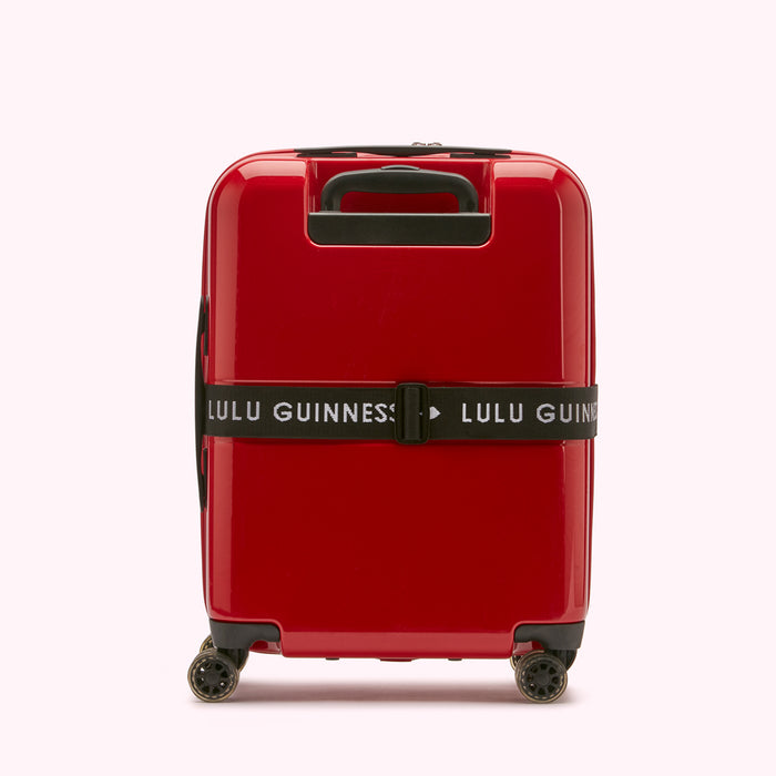 Red Lulu Guinness carry-on suitcase with black luggage strap.