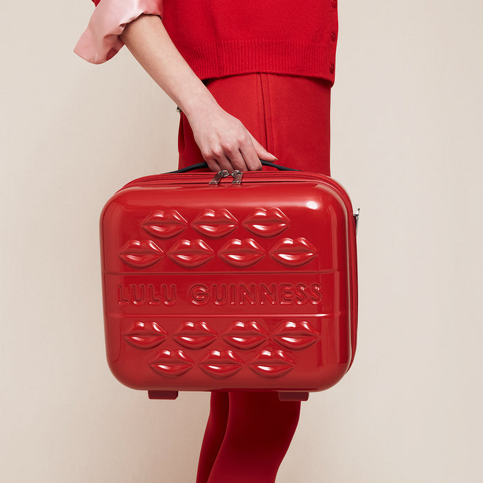 Women in a red outfit holding a red hard shell vanity case with lip details and Lulu Guinness branding.