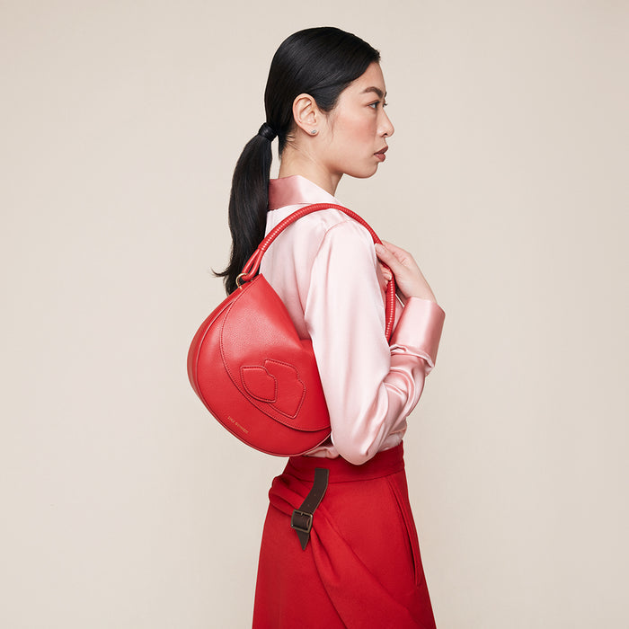 Woman carrying a red leather shoulder bag with a lip design on the front against a beige background