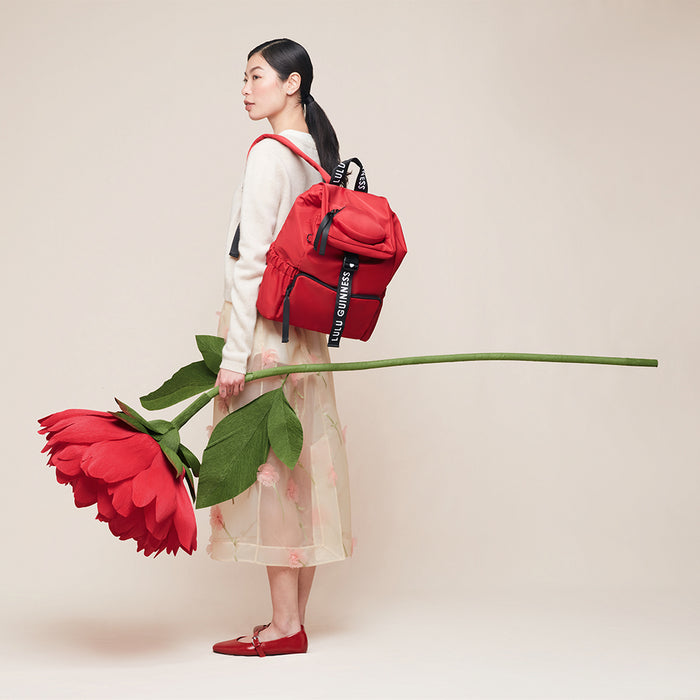 Woman holding a large red flower with a red backpack on a beige background