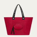Red tote bag with black handles featuring 'Lulu Guinness' and a lip-shaped pocket on a light grey background