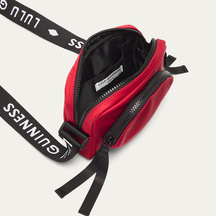 Red crossbody bag with black branded 'Lulu Guinness' strap open on a white background
