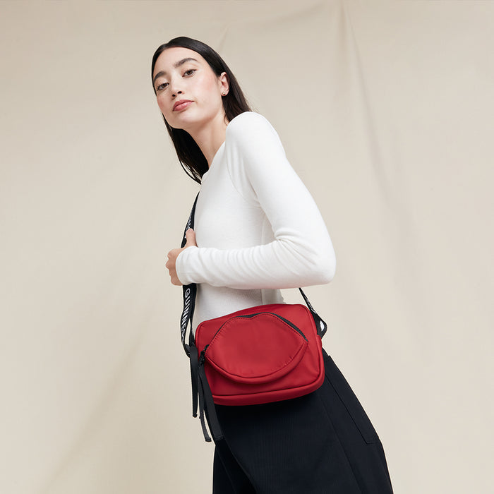 Woman carrying a red crossbody bag with a 'Lulu Guinness' logo against a beige background