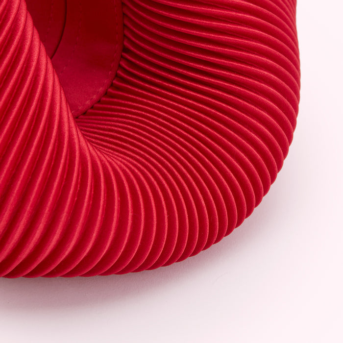 Close-up of a vibrant red fabric with deep, concentric pleats against a white background.