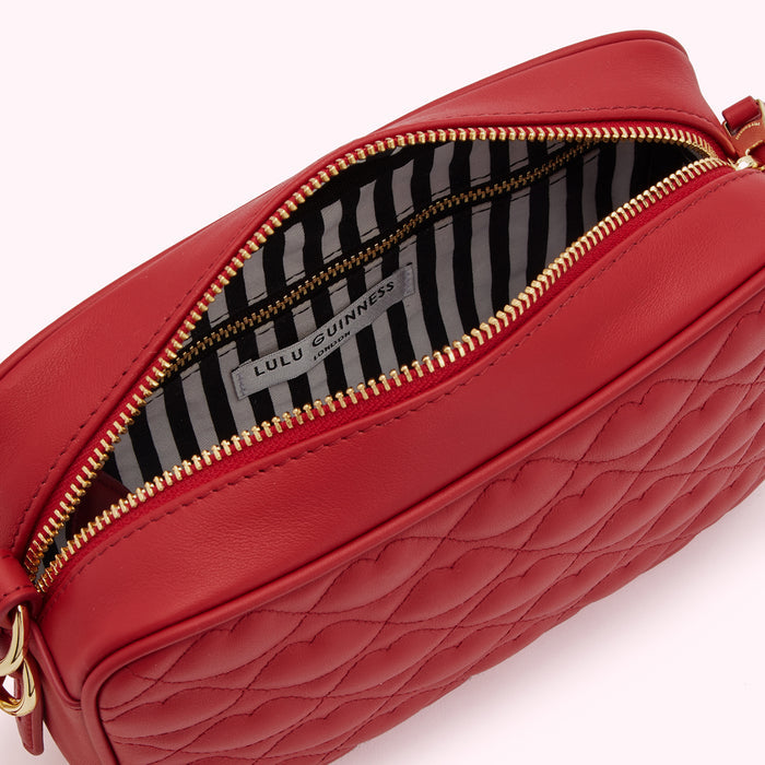 Red quilted Lulu Guinness crossbody bag open to reveal its black and white striped interior.
