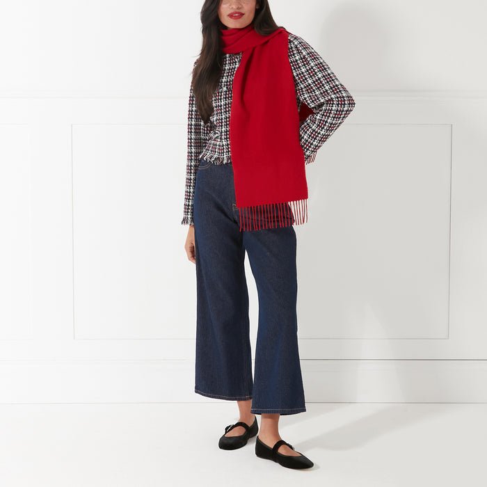 Woman wearing a red scarf, a black and white tweed jacket, dark wash wide-leg jeans, and black flats against a white background.
