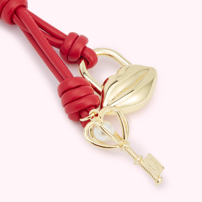 Red leather bracelet with gold lip-shaped padlock and key charm.