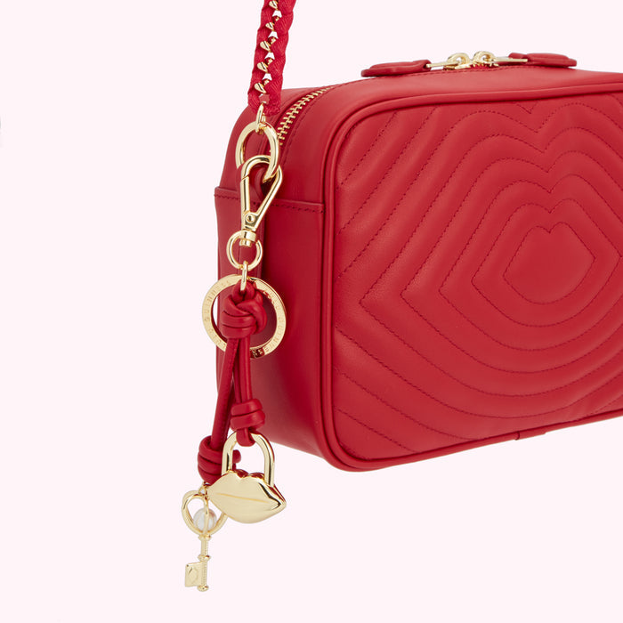Close-up of a red quilted crossbody bag with gold-toned hardware and a lip-shaped charm.