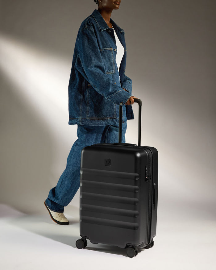 a man in a jean jacket and white sneakers pulling a suitcase
