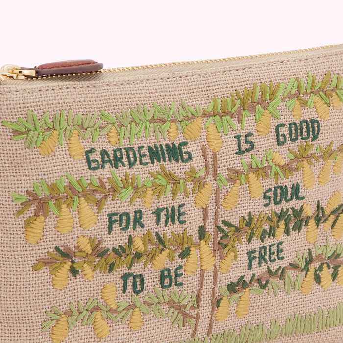 Close-up of a beige canvas pouch with embroidered text and pears reading, "Gardening is good for the soul to be free".