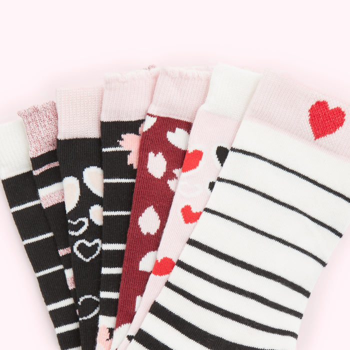 A fan of seven pairs of children's socks with hearts and stripes patterns on a pink background.