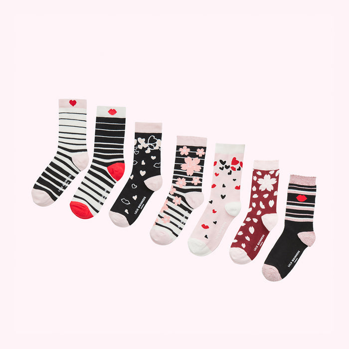 Eight pairs of women's socks in various patterns and colours, including black and white stripes, hearts, lips, and cherry blossoms, arranged on a white background.