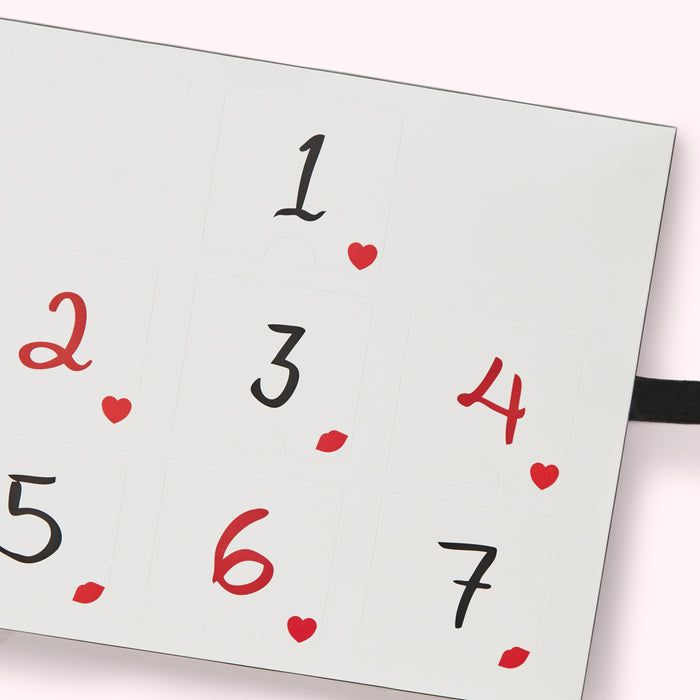 Close-up of a white advent calendar with black numbers 1-7, and red hearts and lips.
