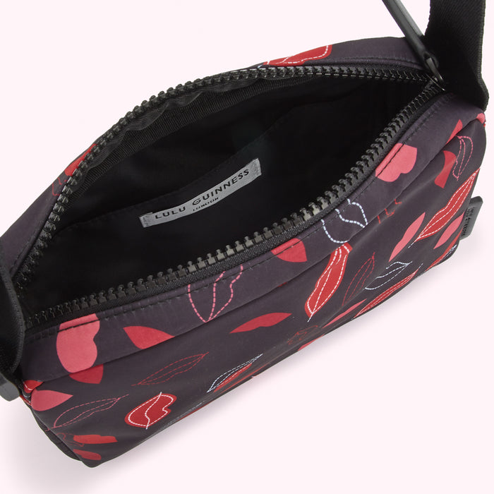 Open Lulu Guinness London crossbody bag with a black background and red and pink lip print.