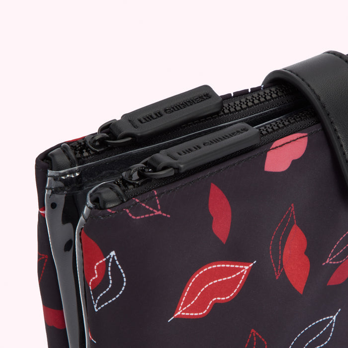 Close-up of a black Lulu Guinness crossbody bag with a red lip print and two zippers.