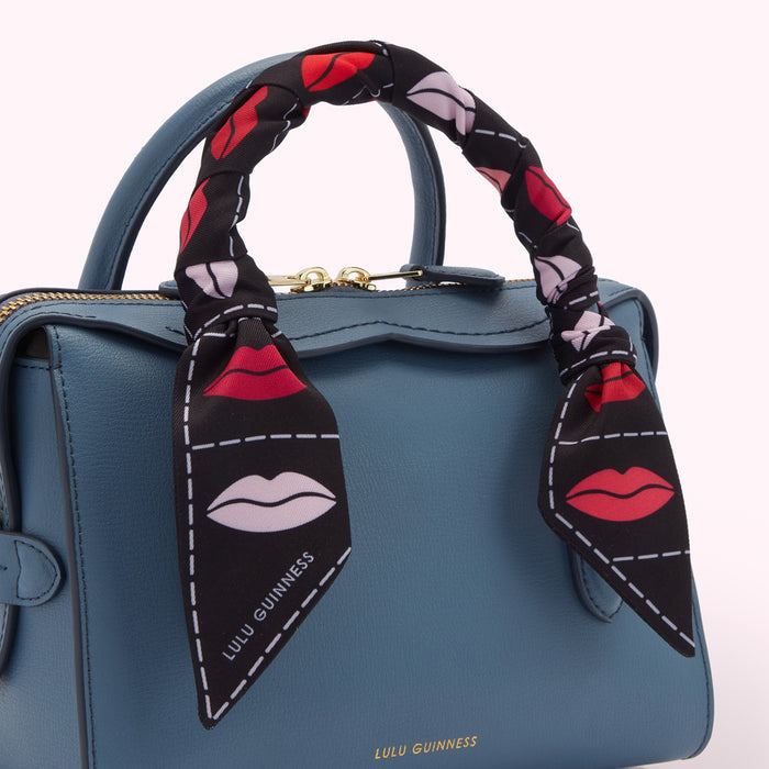 Close-up of a teal Lulu Guinness handbag with a lip-printed scarf tied around the handle.