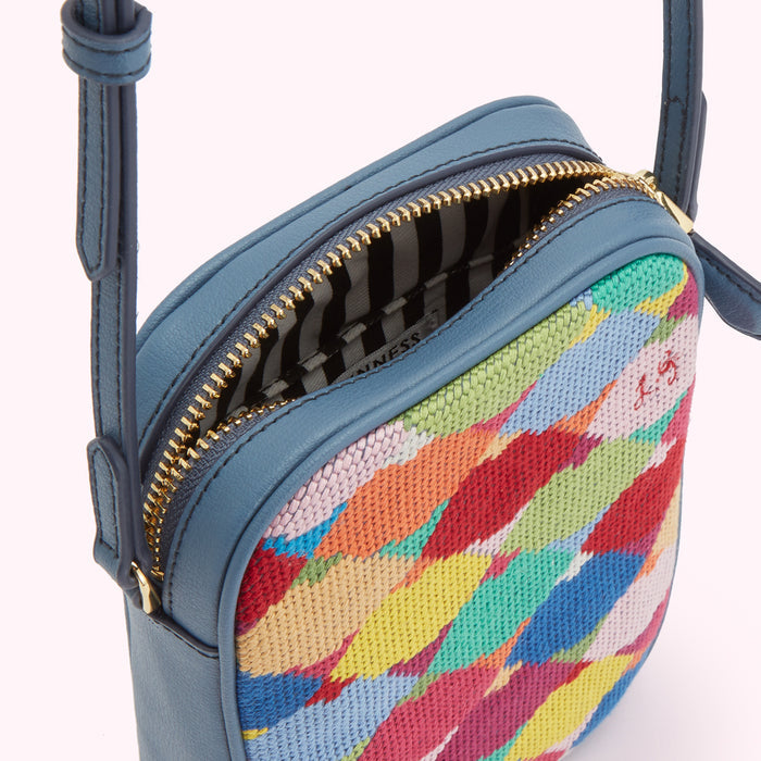 Close-up view of a small, blue crossbody bag with a colourful, abstract pattern. The bag is open, showing its gold zipper and striped interior.