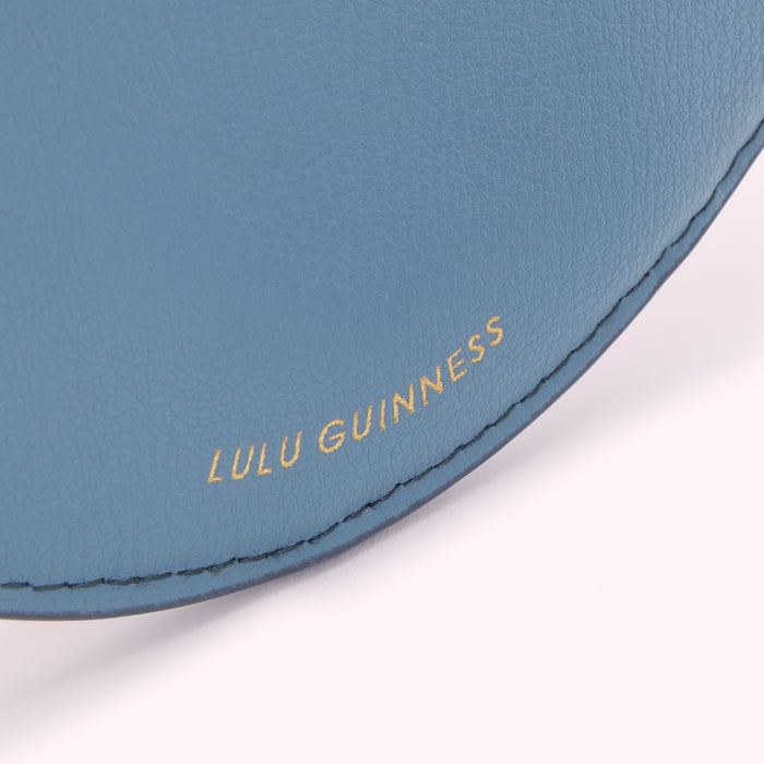 Close-up of a blue Lulu Guinness handbag, showing the brand name embossed in gold.