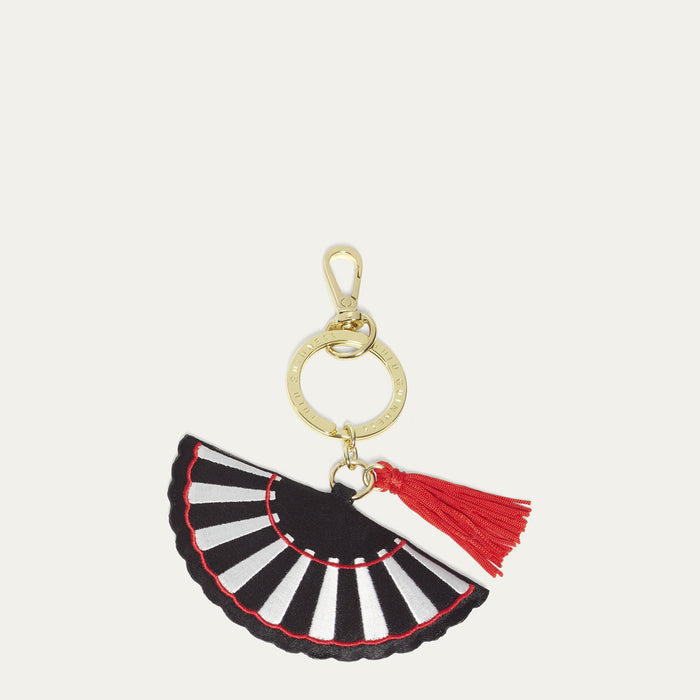 Black and white striped fan shaped keychain with a red tassel on a light gray background