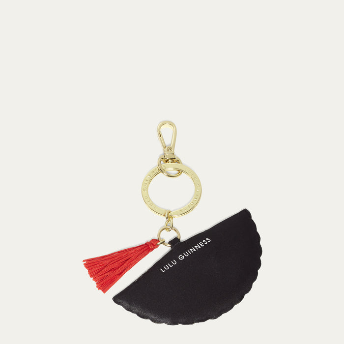 Black fan-shaped keychain with red tassel and gold ring on a white background