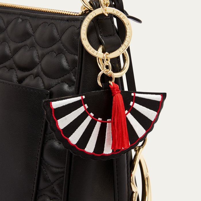 Black quilted handbag with a decorative keychain featuring a black and white striped fan and red tassel.