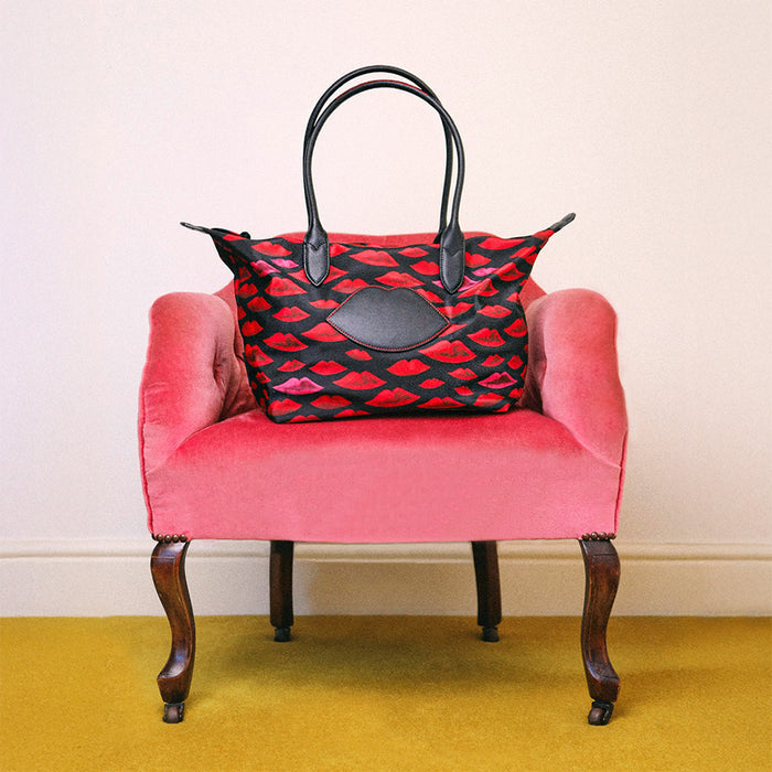 Red and black patterned handbag on a pink chair with a yellow floor and white wall background