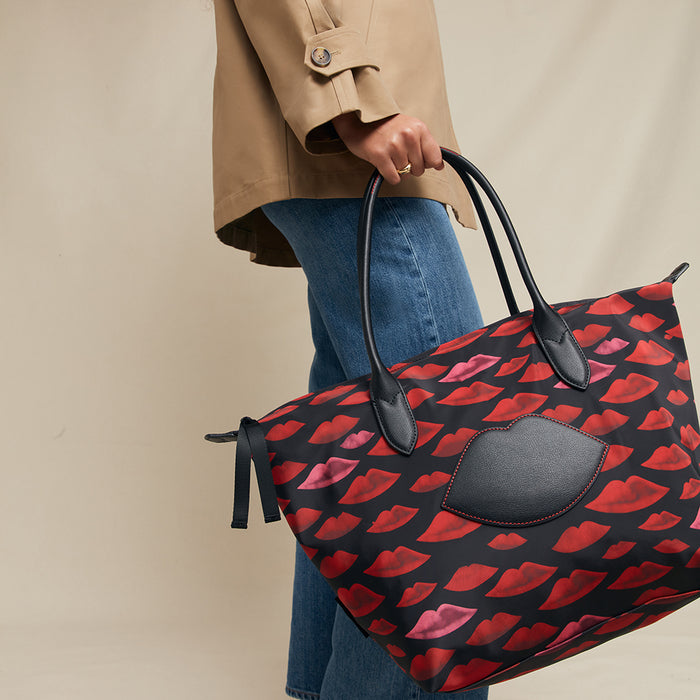 Person holding a large handbag with red lip pattern and black accents against a beige background