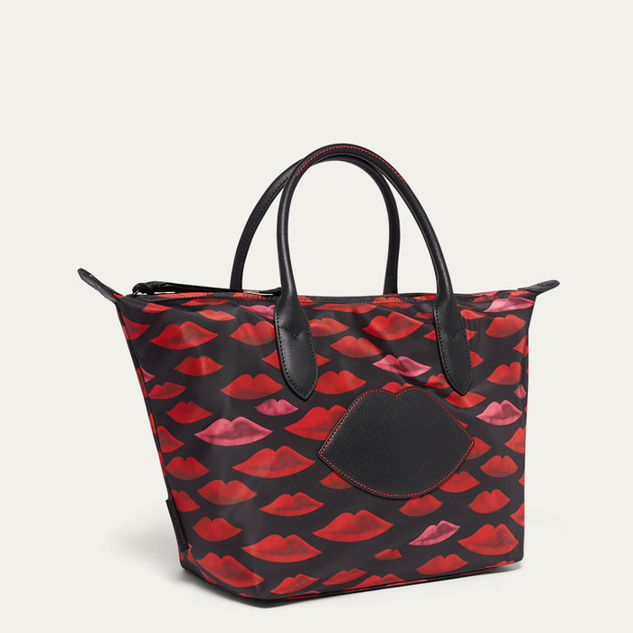 Tote bag with red and pink lip pattern and black leather lip patch on a beige background