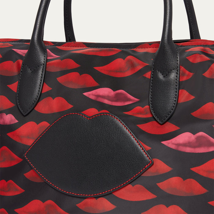 Close up image of a tote bag with red and pink lip pattern and a black leather lip on the front
