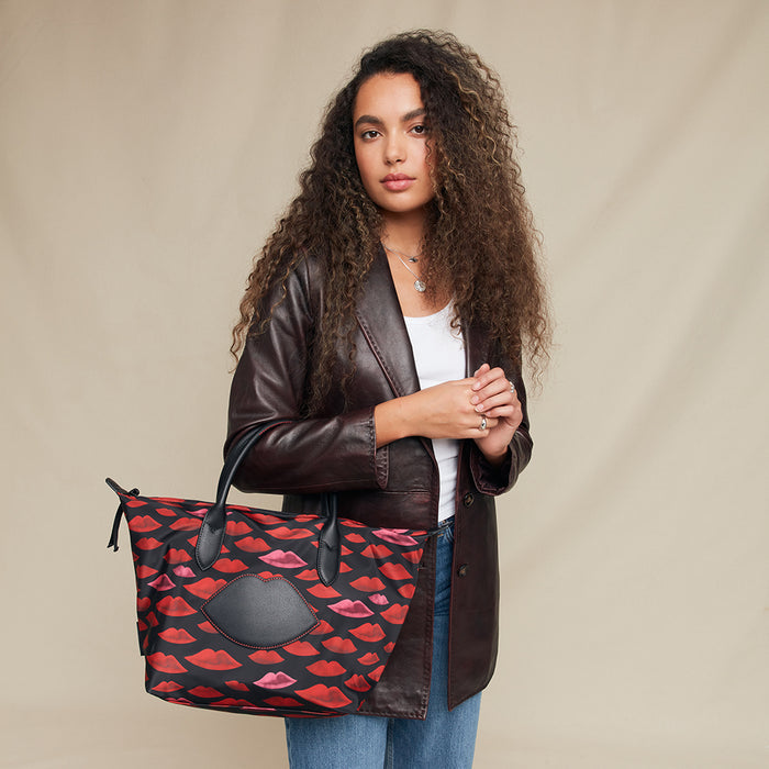 Woman holding a handbag with a red lip pattern against a beige background