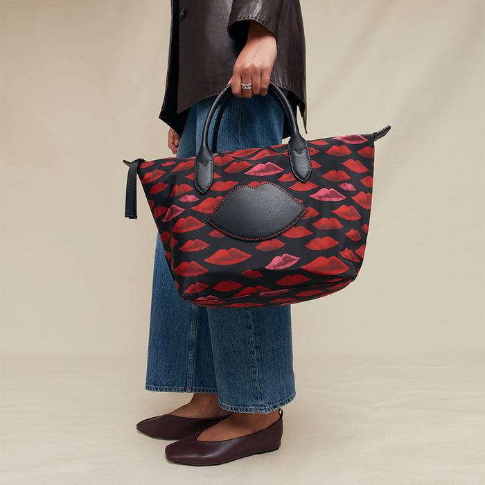 Person holding a red and black lip patterned handbag against a beige background