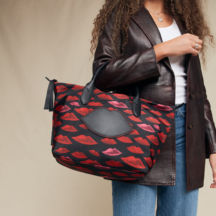 Person holding a red and black lip patterned bag against a beige background