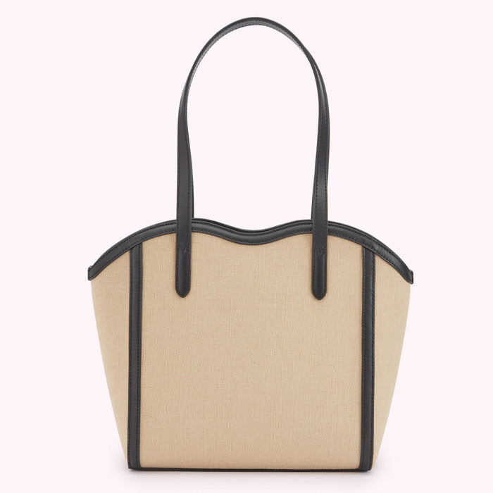 A back image of a beige canvas and black leather tote bag with a curved top and shoulder strap.