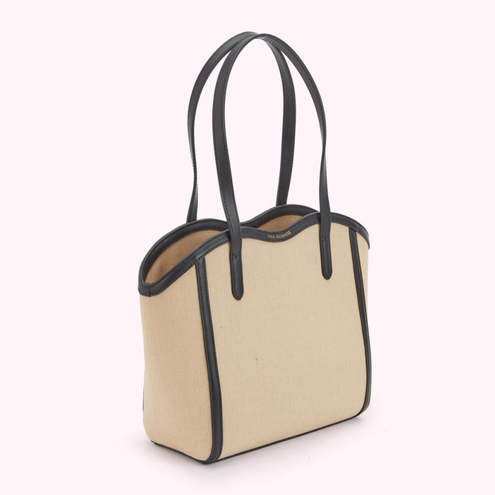 A side image of a beige canvas and black leather tote bag with a curved top and shoulder strap.
