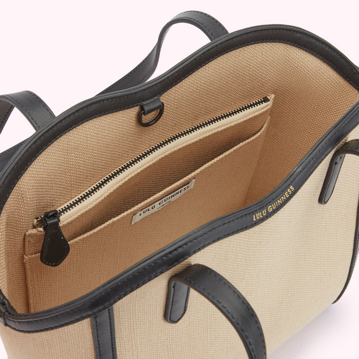 A inside image of a beige canvas and black leather tote bag from above revealing a inside slip pocket and inside zip pocket.