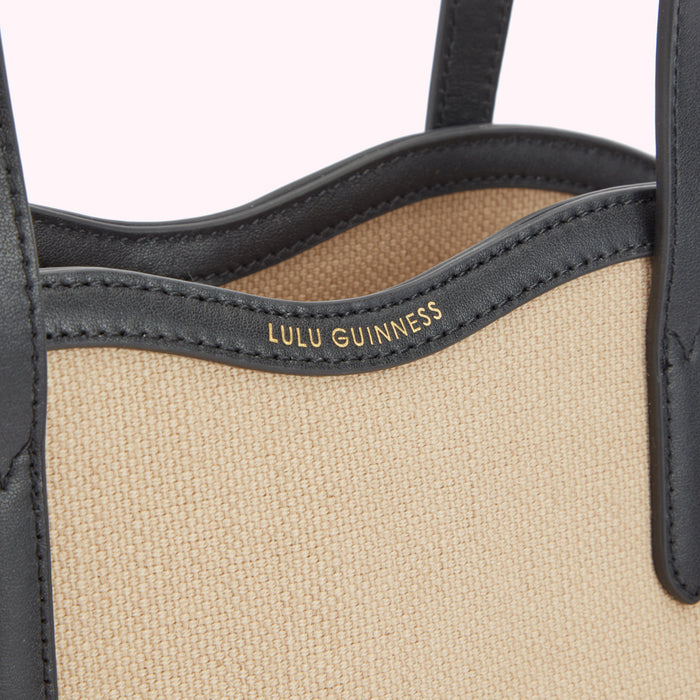 Detail close up image of a beige canvas and black leather tote bags foil print 'Lulu Guinness' logo.