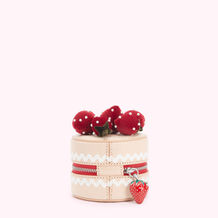 A beige leather cake-shaped purse with red velvet strawberries and a zipper. The background is white.