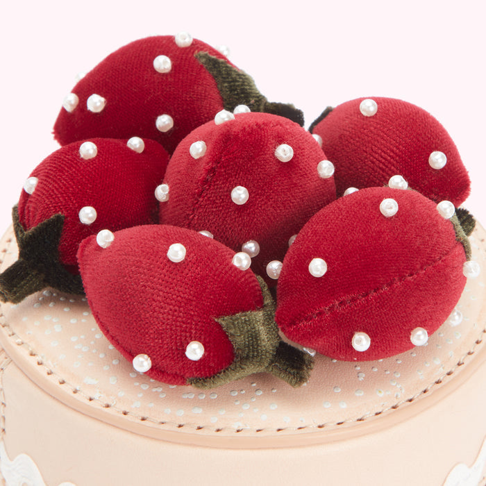 Close-up of a pink cake decorated with red velvet strawberries adorned with pearl accents.
