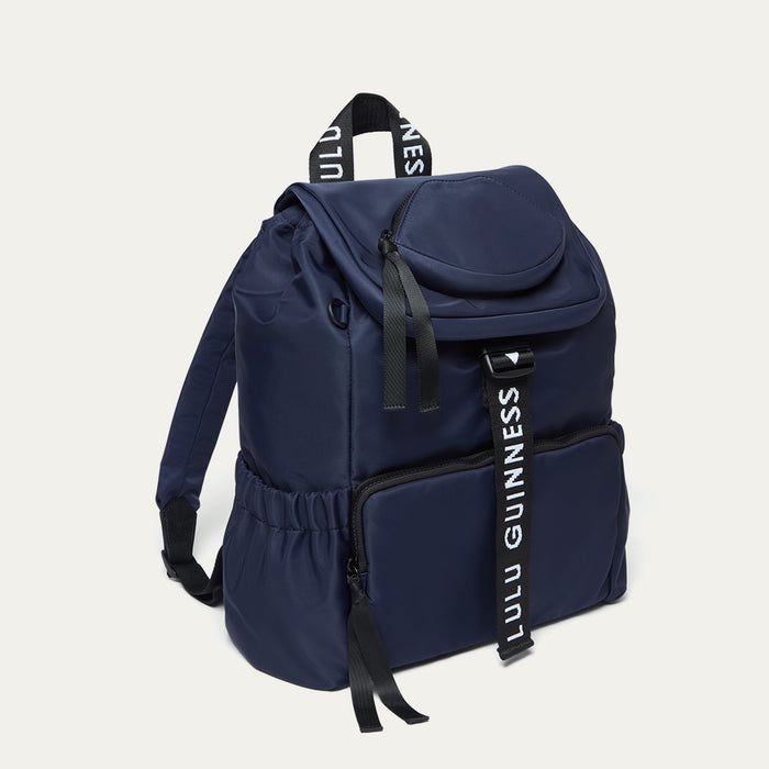Navy blue backpack with black 'Lulu Guinness' straps on a light grey background