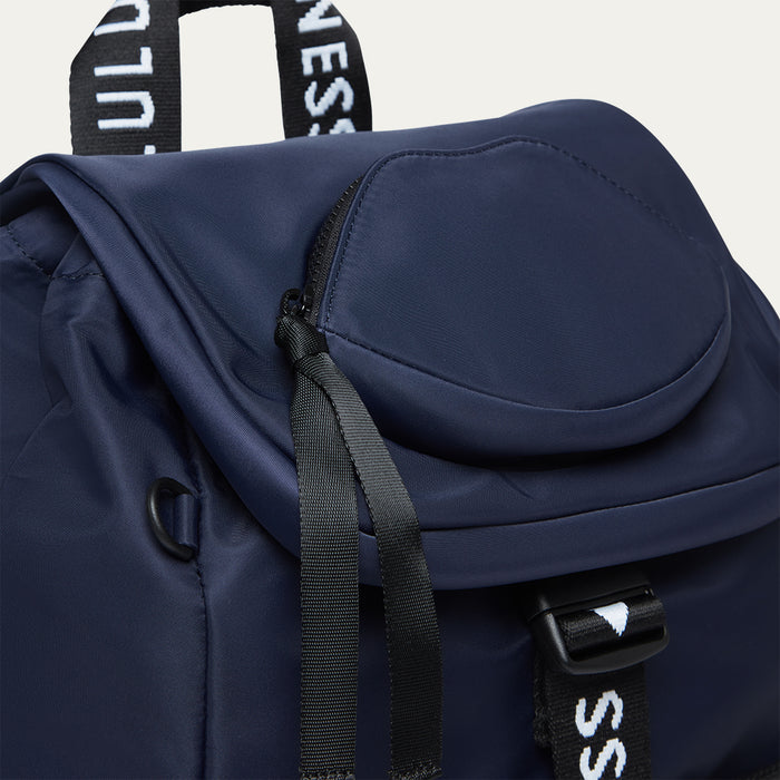 Navy blue backpack with black 'Lulu Guinness' branded straps on a light grey background