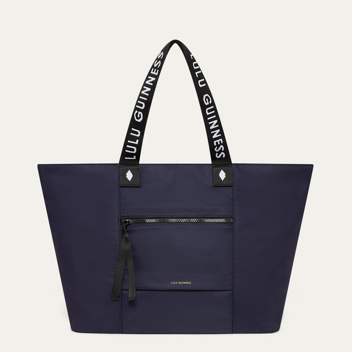 Navy tote bag with black handles featuring 'Lulu Guinness' on a light grey background