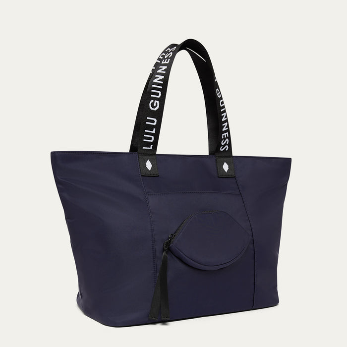 Navy tote bag with black handles featuring 'Lulu Guinness' branding on a light grey background.