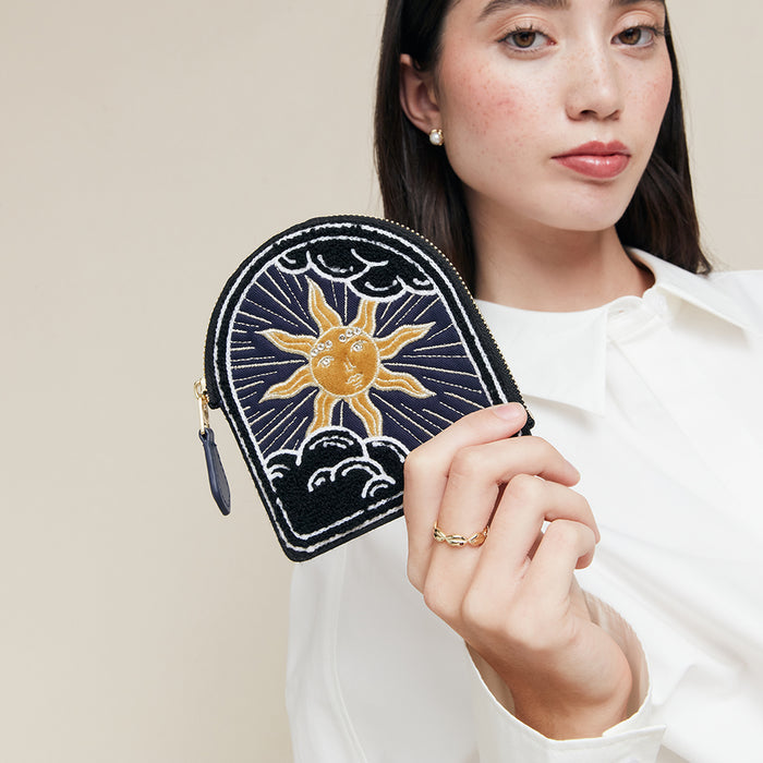 Woman holding a coin purse with a sun design against a beige background