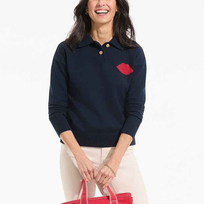 Woman wearing a navy sweater with a red lip design, holding a red bag on a white background