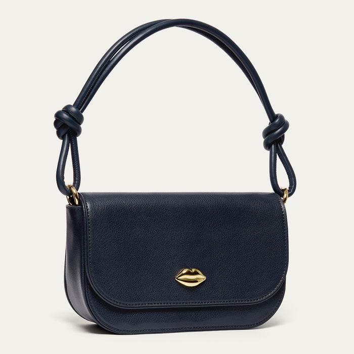 Navy blue leather shoulder bag with a gold lip on the front and a knotted shoulder strap on a light grey background