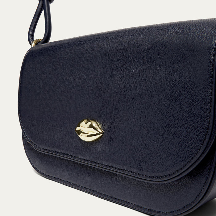 Navy blue leather shoulder bag with a gold lip on the front on a light grey background