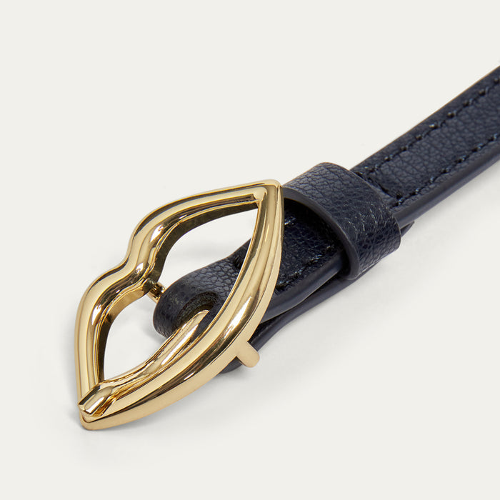 Close up images of a navy leather belt with a gold lip-shaped buckle on a light grey background